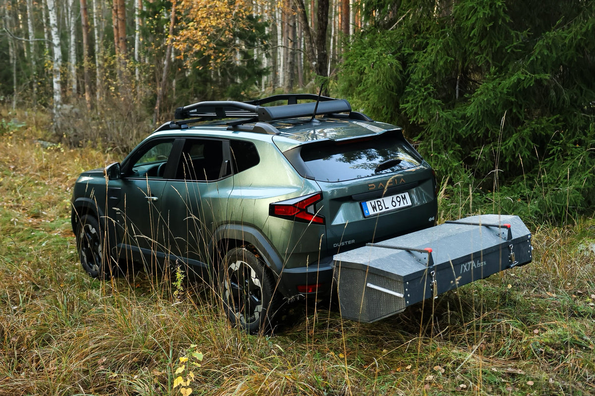 Dacia Duster s namontovaným zadním boxem IXTAbox na tažné zařízení, zaparkovaná na lesní cestě